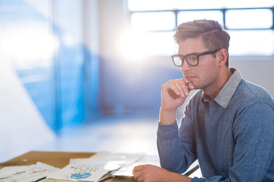 Man wearing glasses collared shirt leaning at desk reviewing charts with pen and laptop, copy space