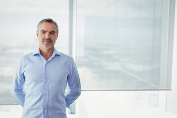 Businessman standing with hands behind back by office window roller blind diffusing cityscape light