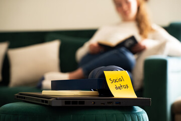 Woman reading book during digital detox, blurred background, laptop, smartphone and headphones with inscription digital detox, stop using digital gadgets, mindfulness and technology break concept