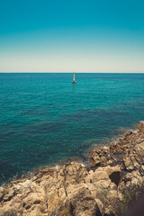 Seascape in Spain with a sailboat in the background and rocky cliffs in the foreground. Costa Brava coast. Vertical view.