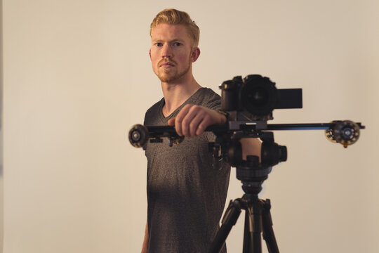 Male camera operator standing behind DSLR camera slider in production studio wearing grey t-shirt