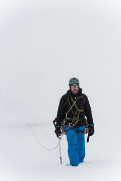 Mid adult man traversing snowy glacier wearing climbing gear and carrying rope and backpack