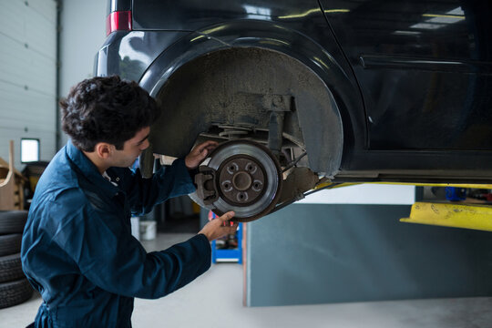 Black SUV on hydraulic lift is getting brake rotor and caliper inspected in garage, copy space
