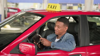 Happy taxi driver holding a wallet with money in his car.