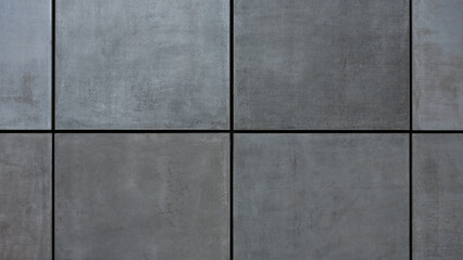 Close-up of a modern concrete wall with large rectangular grey panels separated by narrow black...