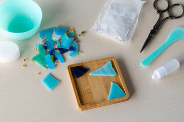 Colorful glass-like fragments prepared for DIY mosaic coaster in silicone mold with gypsum powder and craft tools on table before pouring process begins, step 1