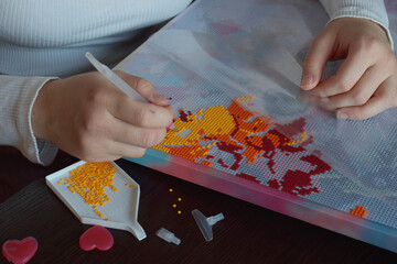 Closeup of hands applying colorful beads to a diamond painting canvas creating a vibrant mosaic...
