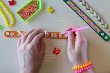 DIY kids bracelet making process with hands decorating plastic wristband using colorful diamond mosaic stickers and craft supplies for creative handmade project