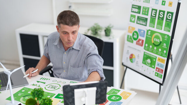 Adult Caucasian man reviewing ESG reports and green business sustainability strategy for carbon reduction and environmental governance in modern office - Powered by Adobe
