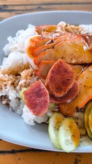 Red pork and crispy pork on rice in a blue plate on a wooden table