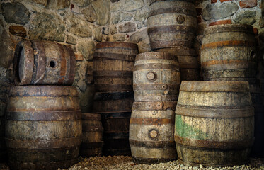 Old wooden barrels stacked against a stone wall in a historic cellar creating an atmosphere of...