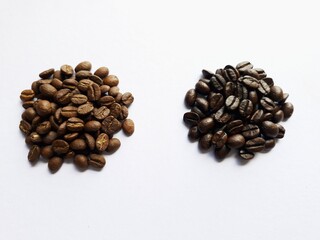 Medium and dark arabica coffee beans are roasted on white paper.