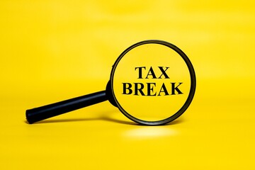 TAX BREAK concept zoomed through a magnifying glass isolated on a yellow background. 