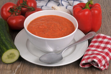 Bol de gaspacho fait maison avec une cuillère et ses ingrédients en gros plan