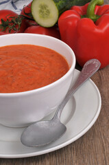 Bol de gaspacho fait maison avec une cuillère et ses ingrédients en gros plan