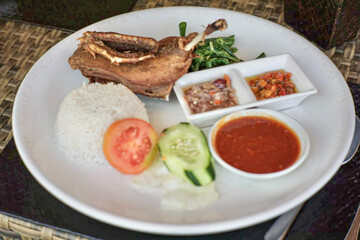 Traditional Indonesian fried duck served with steamed rice, fresh vegetables, and assorted sambal...