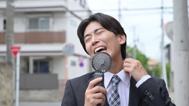 暑い中汗をかく営業する大変なビジネスマン　ハンディファンで涼むイメージ　夏の外回りは熱中症に注意の動画