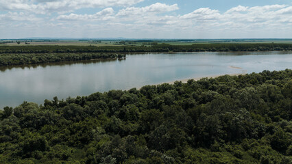 Drone aerial view of the Danube River curving past dense green forest and farmland in Belegis,...