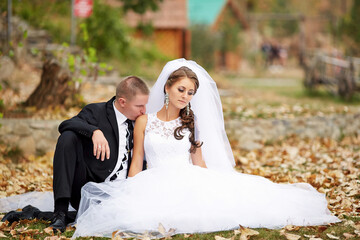 A bride and groom are sitting on the ground in a field