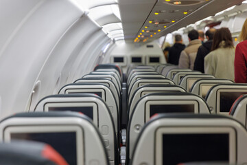 A crowded airport terminal shows passengers lining up to board a plane. The interior features rows of empty seats with personal screens, highlighting travel excitement.