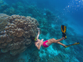 A person snorkeling among colorful coral formations, observing marine life. The clear blue water offers visibility of underwater beauty and a sense of adventure.