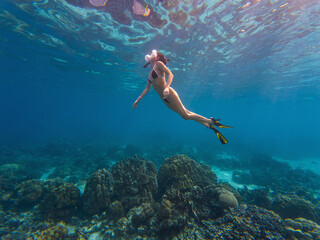 A person enjoys snorkeling in clear turquoise waters above a colorful coral reef, exploring marine life beneath the surface. The sunlight creates a shimmering effect on the water.