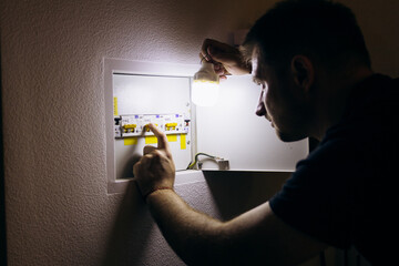 Power outage. A man holds an LED lamp in front of an electrical panel.