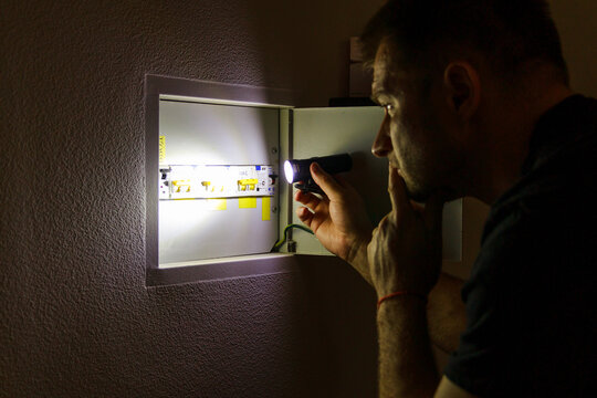Power outage. A man holds an LED lamp in front of an electrical panel.
