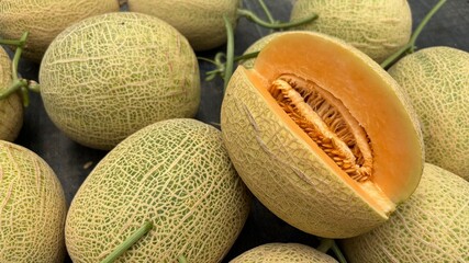 Group of netted melons with one cut open to expose juicy seeds and flesh.