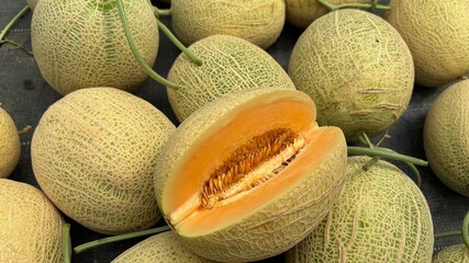 Freshly harvested cantaloupes with one cut open, showcasing juicy orange flesh and seeds.