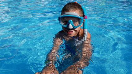 Happy boy swimming in a pool with mask and snorkel, smiling as he swims toward the poolside. Fun summer activity and joyful childhood moment.