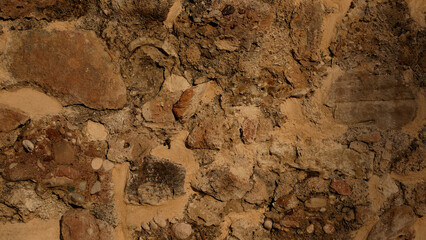 Textured brown stone wall made of large and small stones. Visible structure of clay between the stones. Ancient building material background.