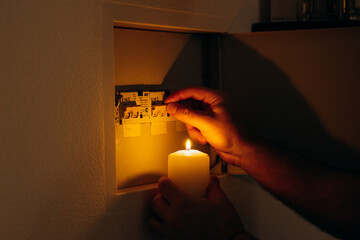 Power outage. A man holds a candle in front of an electrical panel.