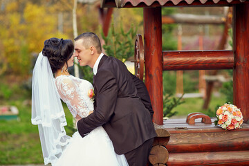 A bride and groom are kissing in front of a wooden well
