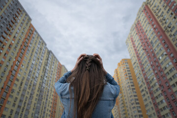 In an urban environment, a young woman with long hair stands with her back to the camera, hands on...