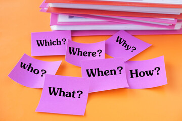 Pink flashcards with English question words—What, When, Where, Why, Who, Which, How—placed on vibrant orange background beside document folders. Educational concept for teaching basic English question