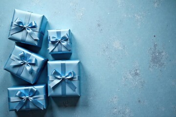 A cluster of light blue gift boxes tied with matching ribbons, arranged on a textured pastel blue background provides ample space for your message