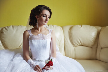 A woman in a white dress sits on a couch with a red flower in her hand