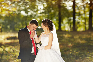 A bride and groom are standing in a field, with the bride wearing a white dress