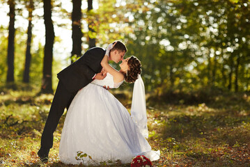 A bride and groom are kissing in the woods