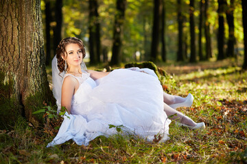 A woman in a white dress is sitting on the ground in a forest