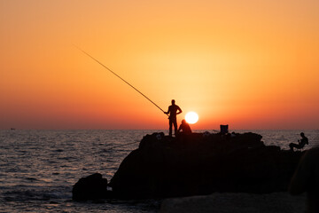 fishermen fishing in the evening by the sea on the Mediterranean sea coast of Caesarea in Israel at sunset time in the direction of the setting sun. High quality photo