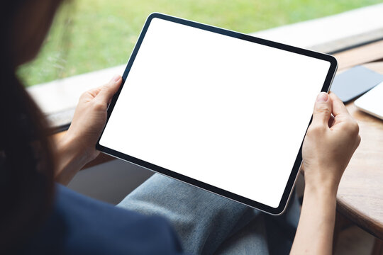 Mockup balnk screen digital tablet. Woman holding digital tablet with blank white screen with laptop computer on table at coffee shop, template for web app design or social media marketing - Powered by Adobe