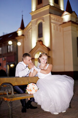 Fototapeta premium A bride and groom are sitting on a bench outside a church