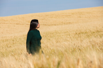 A beautiful, dark-haired teenage Latin girl dressed in green stands among a dry, yellow wheat field on a summer day. In the background, the blue sky.