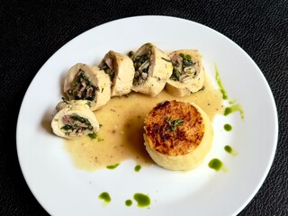 Stuffed chicken roulade with creamy mashed potato and gravy on white plate