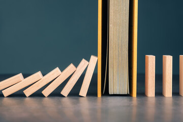 Book blocking falling dominoes, symbolizing knowledge, education, learning, and information as...