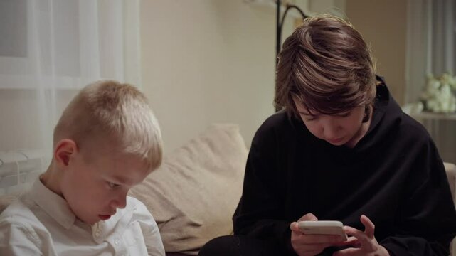 Young mother and her son wearing hearing aids share popcorn while laughing at a TV show. Warm living room scene showcasing joyful family bonding and inclusive representation. Focus on normalizing assi