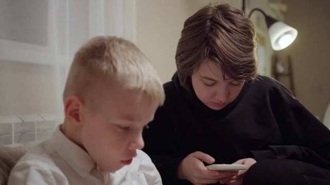 Young mother and her son wearing hearing aids share popcorn while laughing at a TV show. Warm living room scene showcasing joyful family bonding and inclusive representation. Focus on normalizing assi