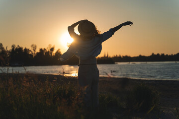 Fototapeta premium Summer portrait of a woman at sunset on the river bank in the glow of the sun